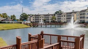 A waterfront hotel with a wooden deck, a fountain, and a row of buildings in the background. - Cozy 1-bedroom studio in peaceful Myrtle Beach w/ AC, indoor, outdoor pool& more (Myrtle Beach)