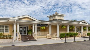 A hotel with a traditional architectural style, featuring a central entrance with steps, a covered porch, and a small tower-like structure on the right. - Cozy 1-bedroom studio in peaceful Myrtle Beach w/ AC, indoor, outdoor pool& more (Myrtle Beach)