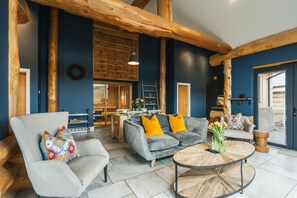 A spacious living area with a grey sofa, a round coffee table, and a wooden ceiling. - The Farmhouse (Ilkley)