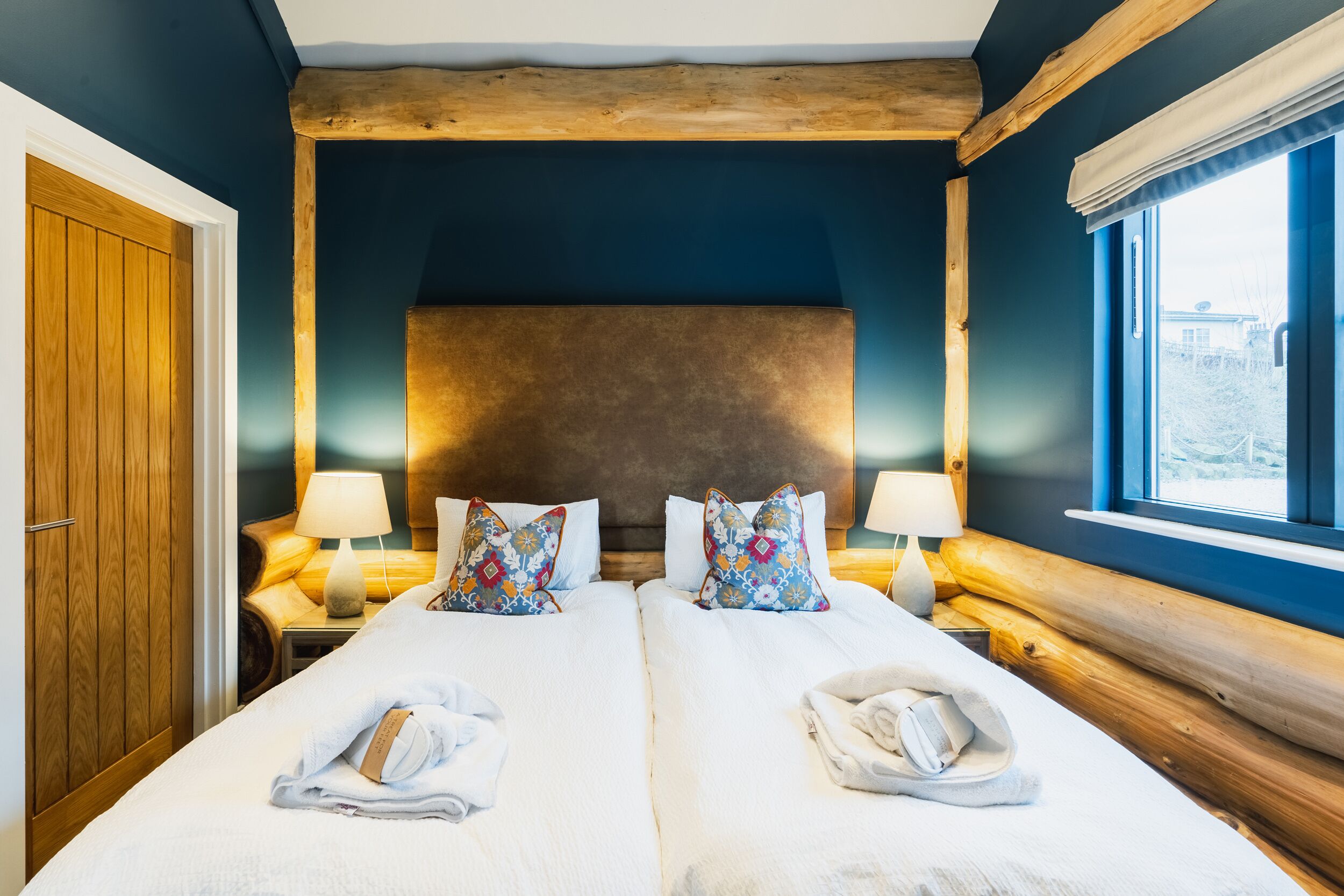 A double room with two beds, wooden headboard, bedside lamps, and a window with a view.