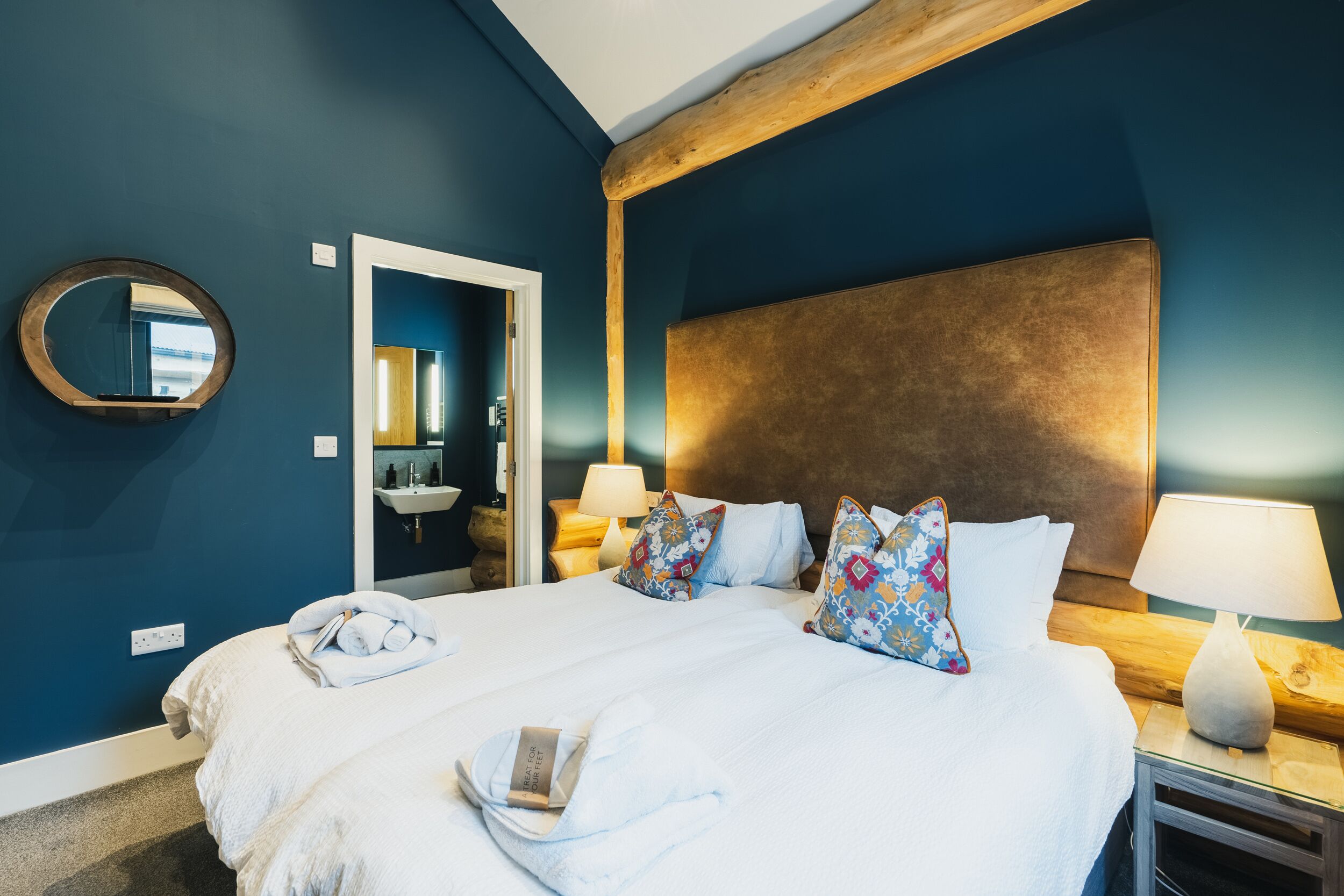 A neatly made bed with white linens and decorative pillows, a bedside table with a lamp, and a wooden headboard.