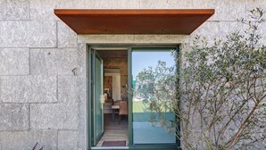 A modern building entrance with a glass door, a stone wall, and a wooden overhang. - Apartment 'T2 Familiar Ua02' with Shared Pool, Wi-Fi and Air Conditioning (Palmeira)