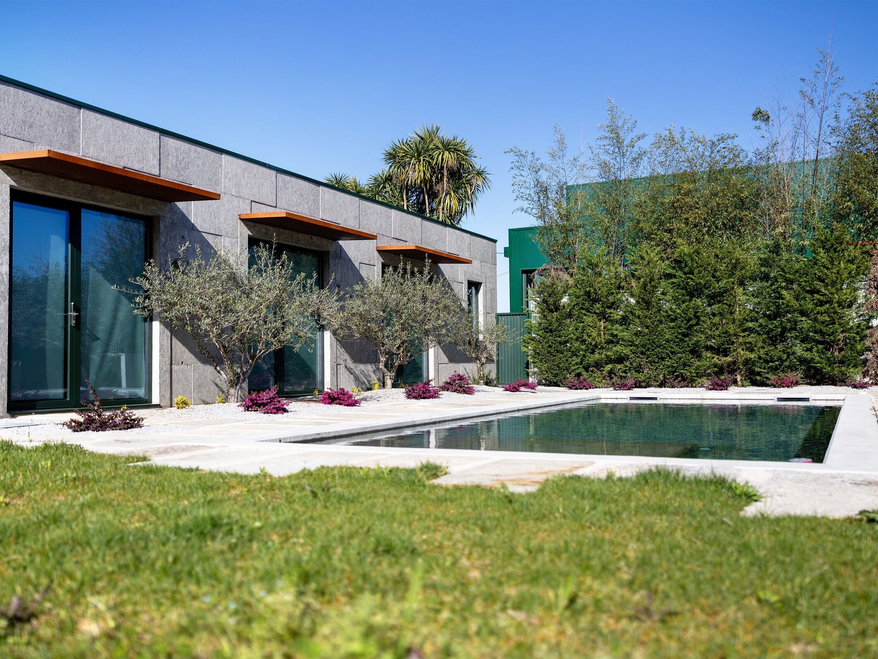 A modern building with large windows, a swimming pool, and a well-maintained garden.