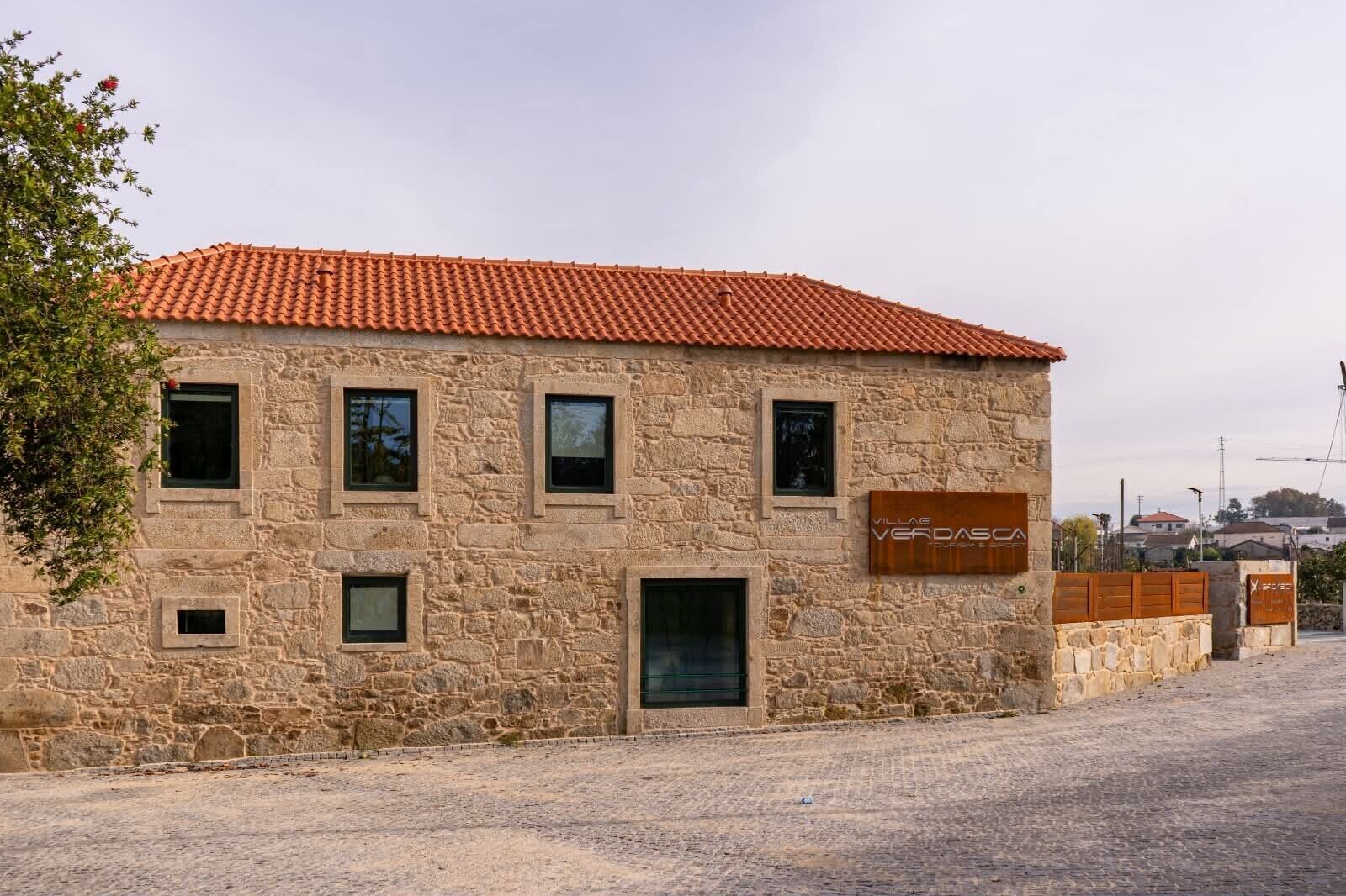 Un edificio de piedra con techo de tejas, varias ventanas y un cartel.
