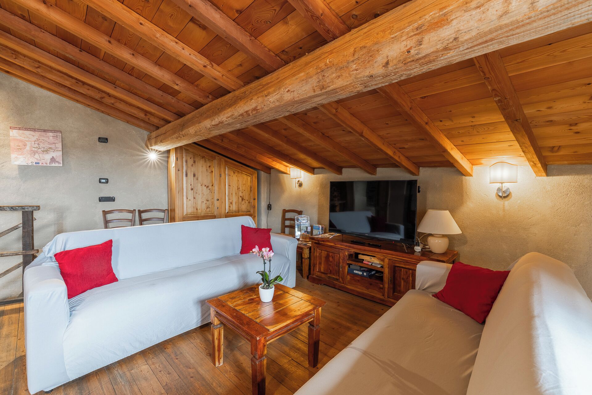 A cozy living room with wooden beams, a sofa, a coffee table, and a television.