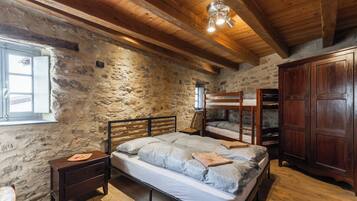 Un dormitorio rústico con pared de piedra, vigas de madera en el techo, una litera, un armario de madera y una mesita de noche con lámpara.