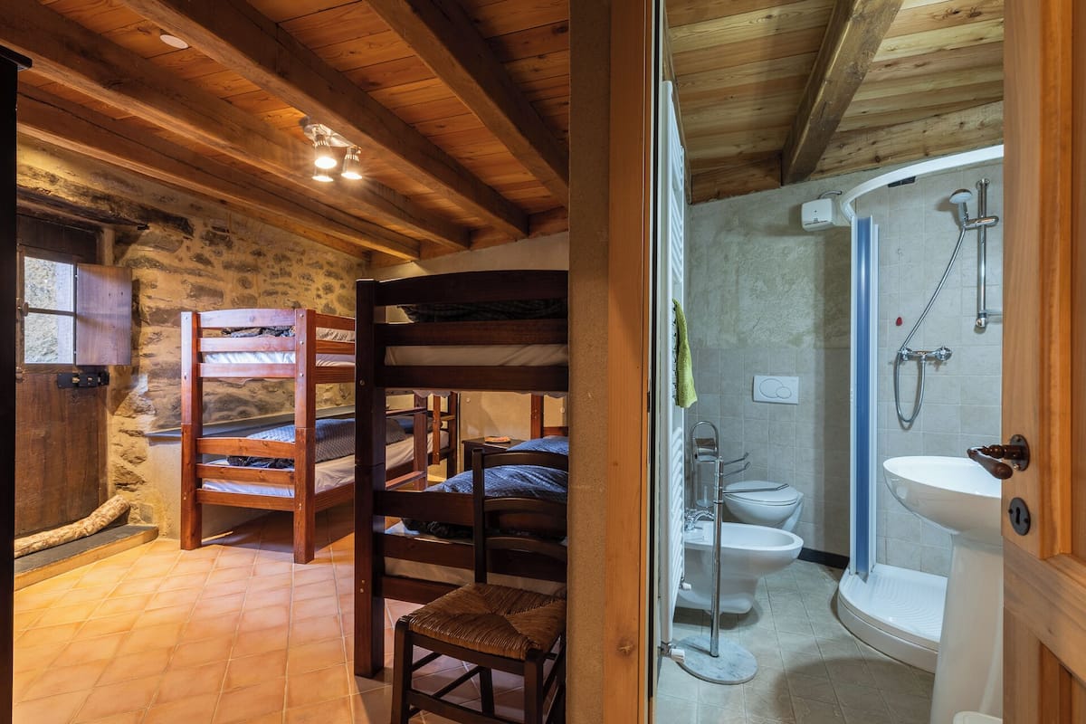 Un interior rústico de madera con literas, un baño con ducha y una pared de piedra.