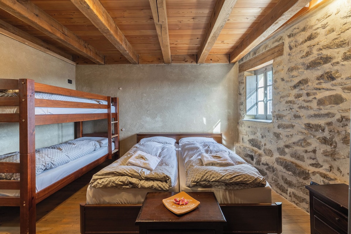 Una habitación con dos literas, una pared de piedra, una ventana y una mesa de madera con un arreglo floral.