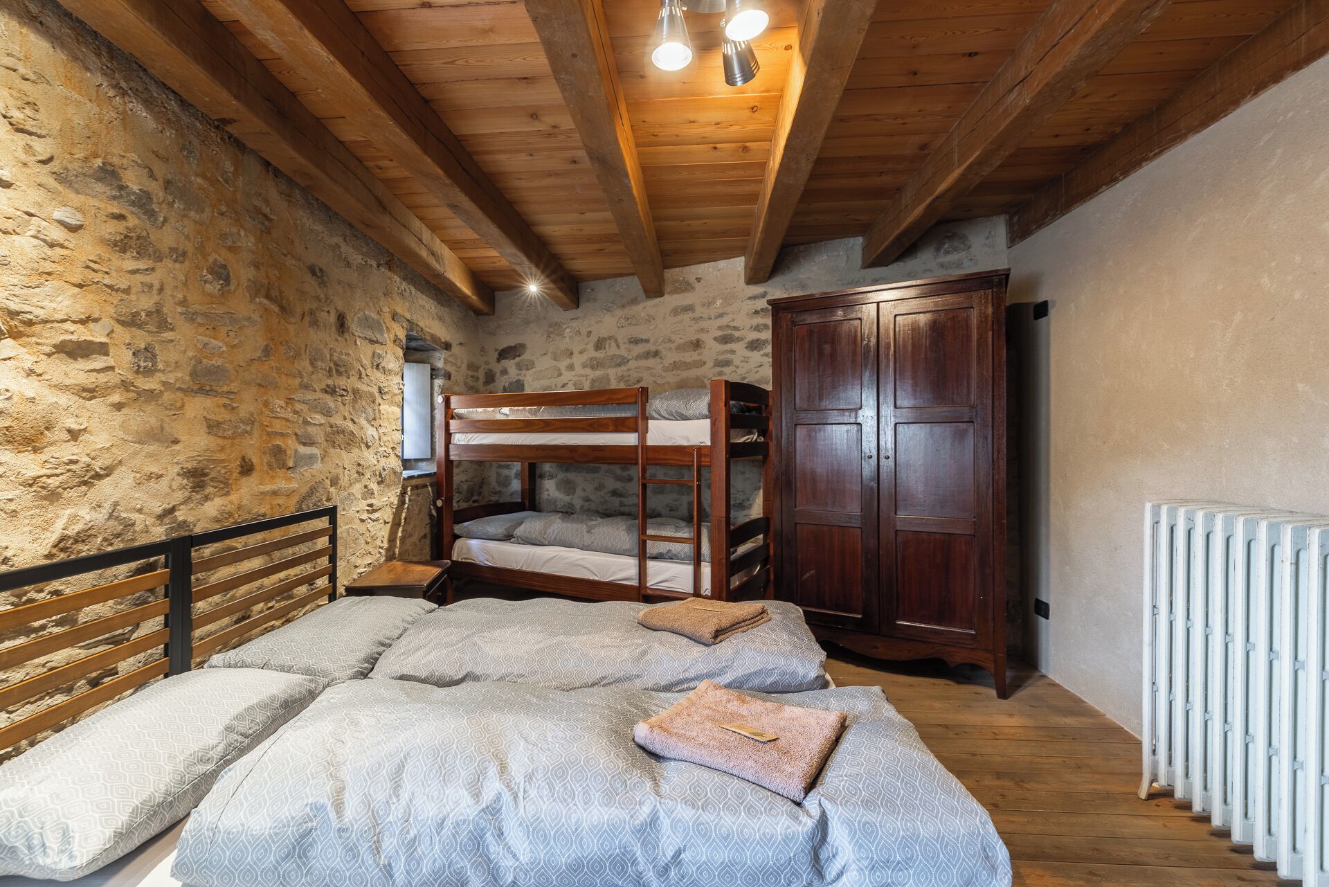 A rustic room with a bunk bed, a wooden wardrobe, and a radiator.