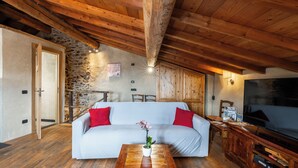 Ein gemütliches Wohnzimmer mit einem weißen Sofa, roten Kissen, einem Holztisch und einem Fernseher.