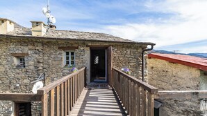 Ein Steinhaus mit einer Holztreppe, die zu einem offenen Durchgang führt.