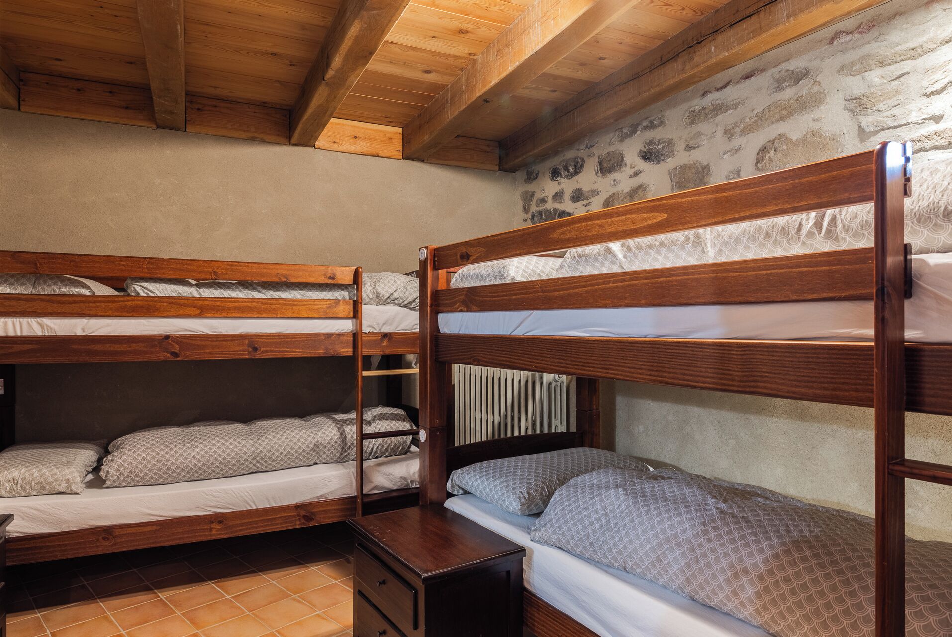 Dormitorio con literas, vigas de madera, paredes de piedra y suelo de baldosas.