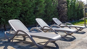 Three sun loungers with a curved design, positioned on a stone surface with a backdrop of dense green foliage. - Double Room Ua06 with Shared Pool, Wi-Fi and Air Conditioning (Palmeira)