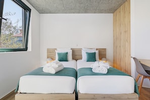 A room with two beds, each with a green bedspread and white pillows, a wooden headboard, a desk with a chair, and a window with a view of trees and a building. - Double Room Ua07 with Shared Pool, Wi-Fi and Air Conditioning (Palmeira)