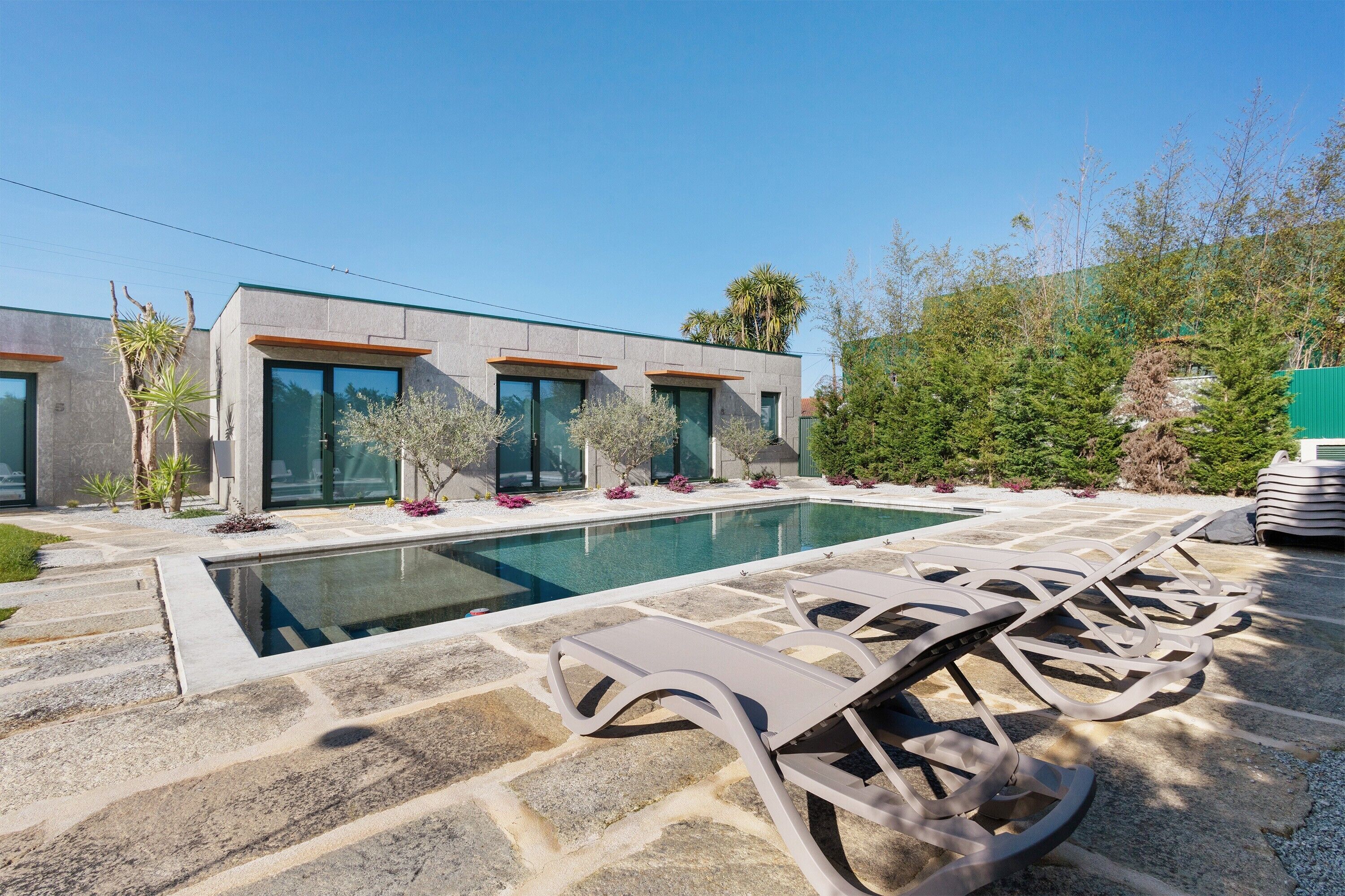 A modern house with a swimming pool, stone patio, and lounge chairs.