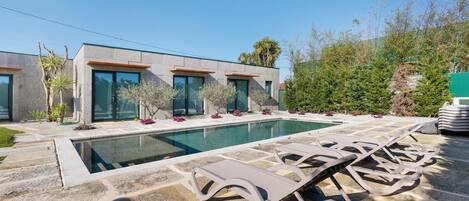 A modern house with a swimming pool, stone patio, and lounge chairs.