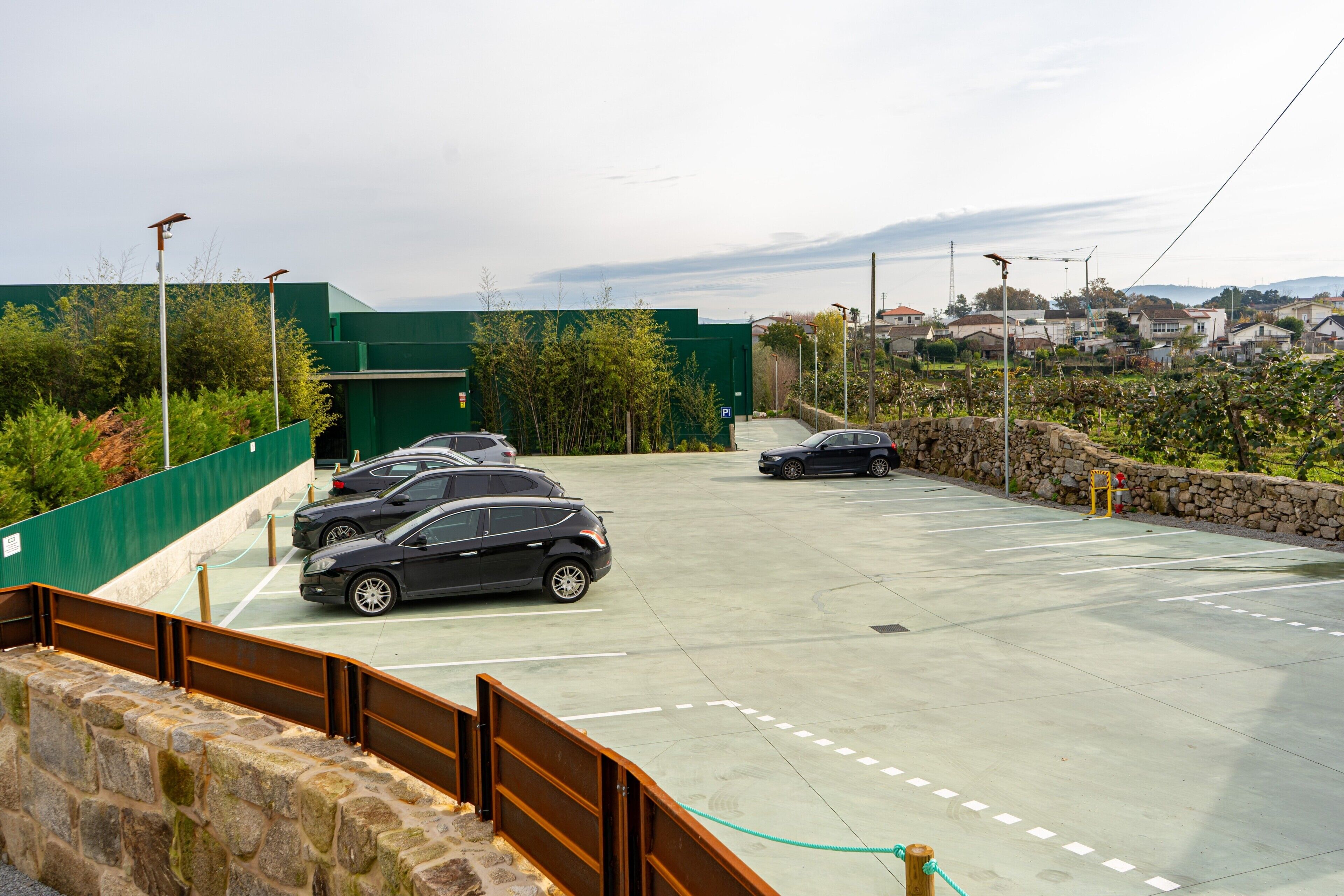 Un estacionamiento con varios coches, un edificio verde y un muro de piedra.