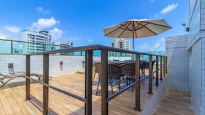 Terraza en la azotea con barandilla de cristal, mobiliario exterior y un gran paraguas.