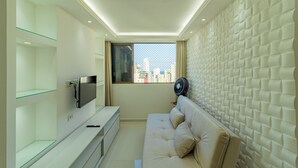 Una sala de estar moderna con un sofá, un televisor de pantalla plana y un ventanal con vista a la ciudad.