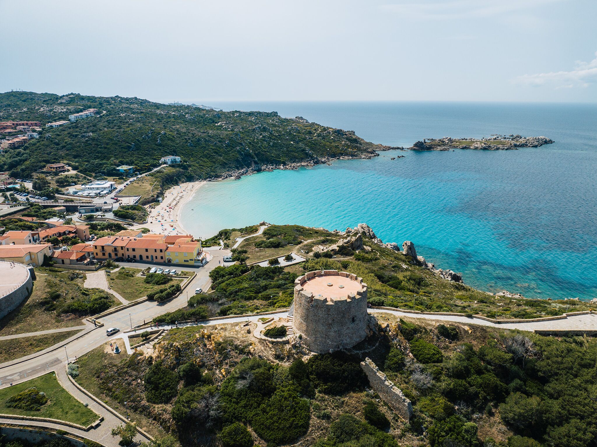 A coastal town with a prominent tower, a beach, and surrounding greenery.