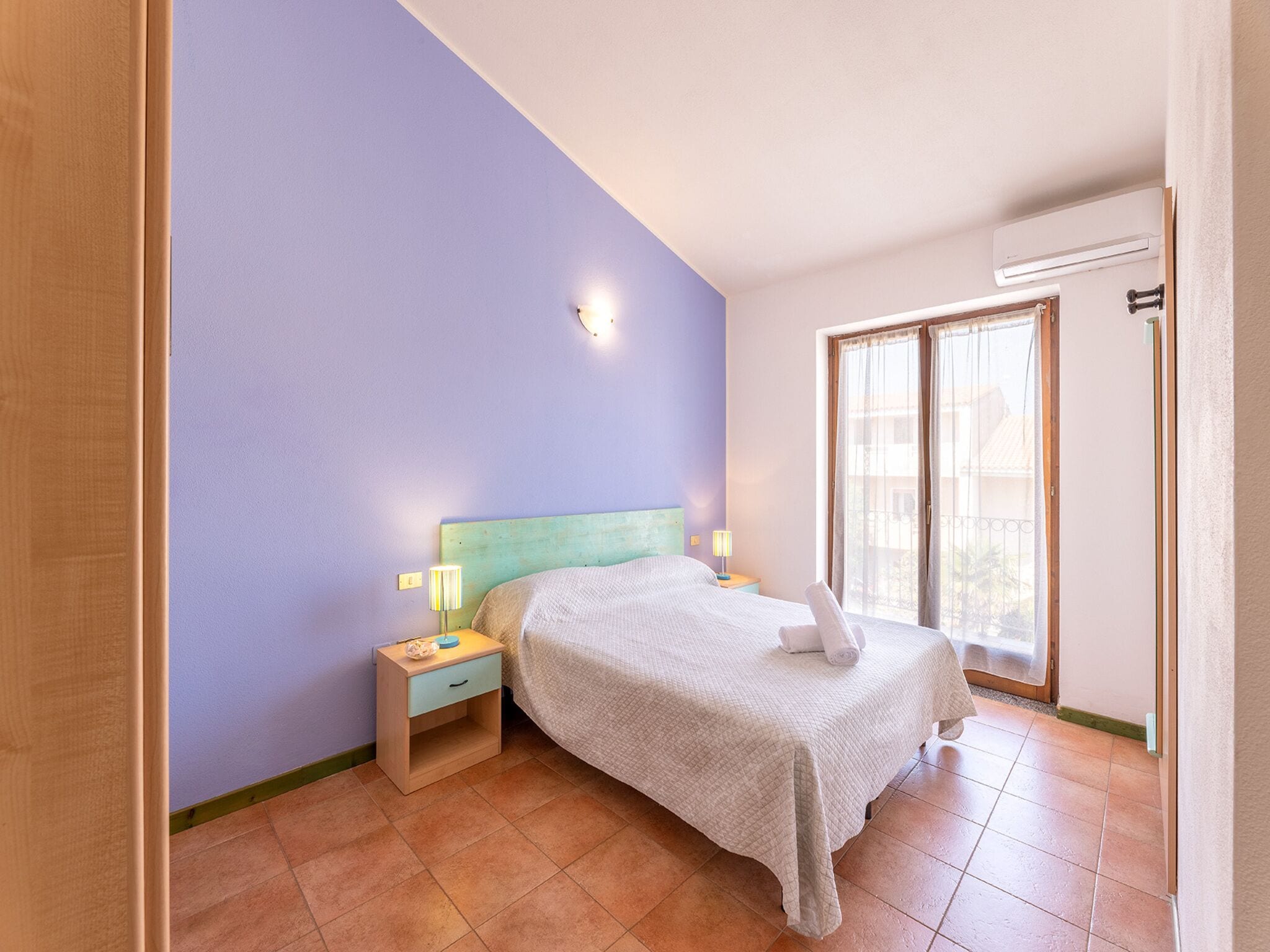 A bedroom with a bed, nightstands, a window, and a door.