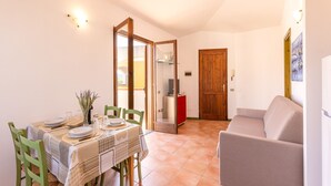 A dining area with a table set for four, a sofa, and a wooden door. - Accommodation 1 km From the Beach (Santa Teresa di Gallura)