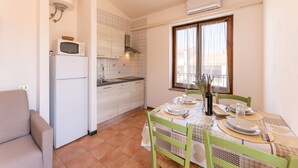 A compact kitchen with a refrigerator, microwave, and stove. There is a dining table with chairs and a window with curtains. - Accommodation 1 km From the Beach (Santa Teresa di Gallura)