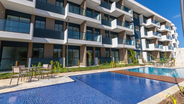 A modern hotel with multiple balconies, a swimming pool, and outdoor seating. - Makia Beach #b12 - em Muro Alto por Carpediem (Ipojuca)
