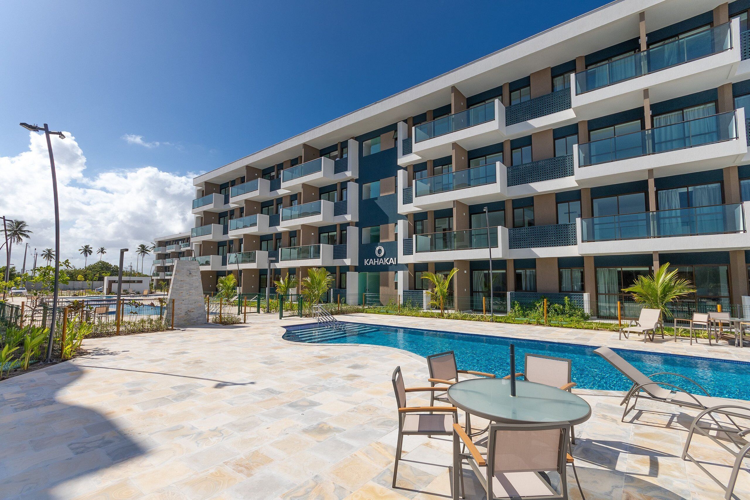 Un hôtel moderne doté d’une piscine, d’un espace extérieur aménagé et offrant une vue sur un ciel d’un bleu éclatant.