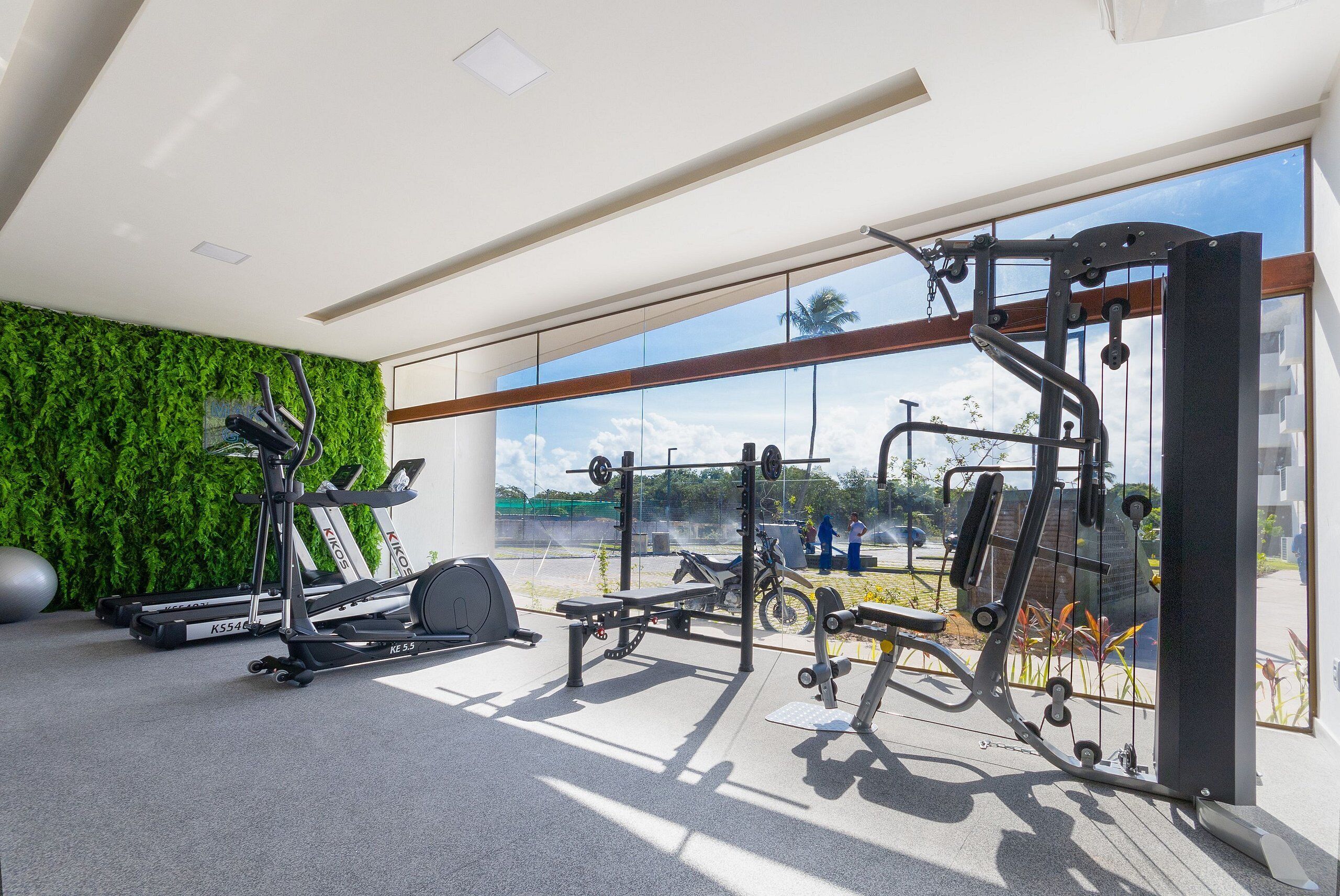Uma academia com equipamentos de exercícios, uma parede verde e uma grande janela com vista para o exterior.