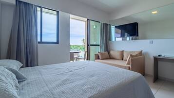 Quarto de hotel com uma cama grande, um sofá, uma TV na parede e uma varanda com vista.
