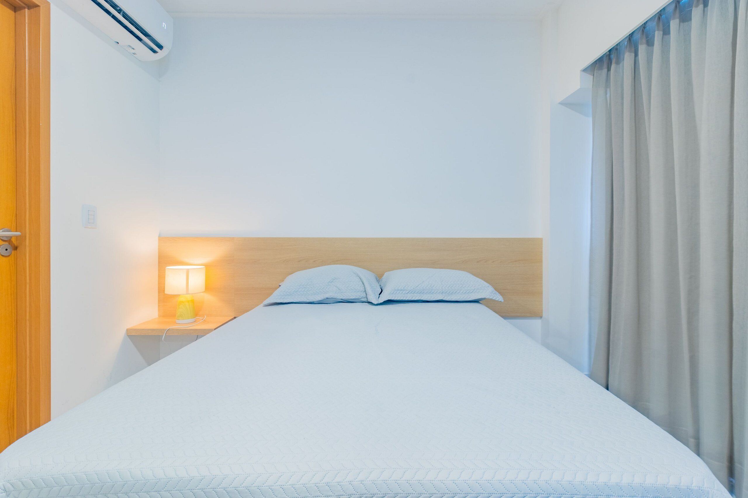 A neatly made bed with a wooden headboard, a bedside lamp, and a window with curtains.