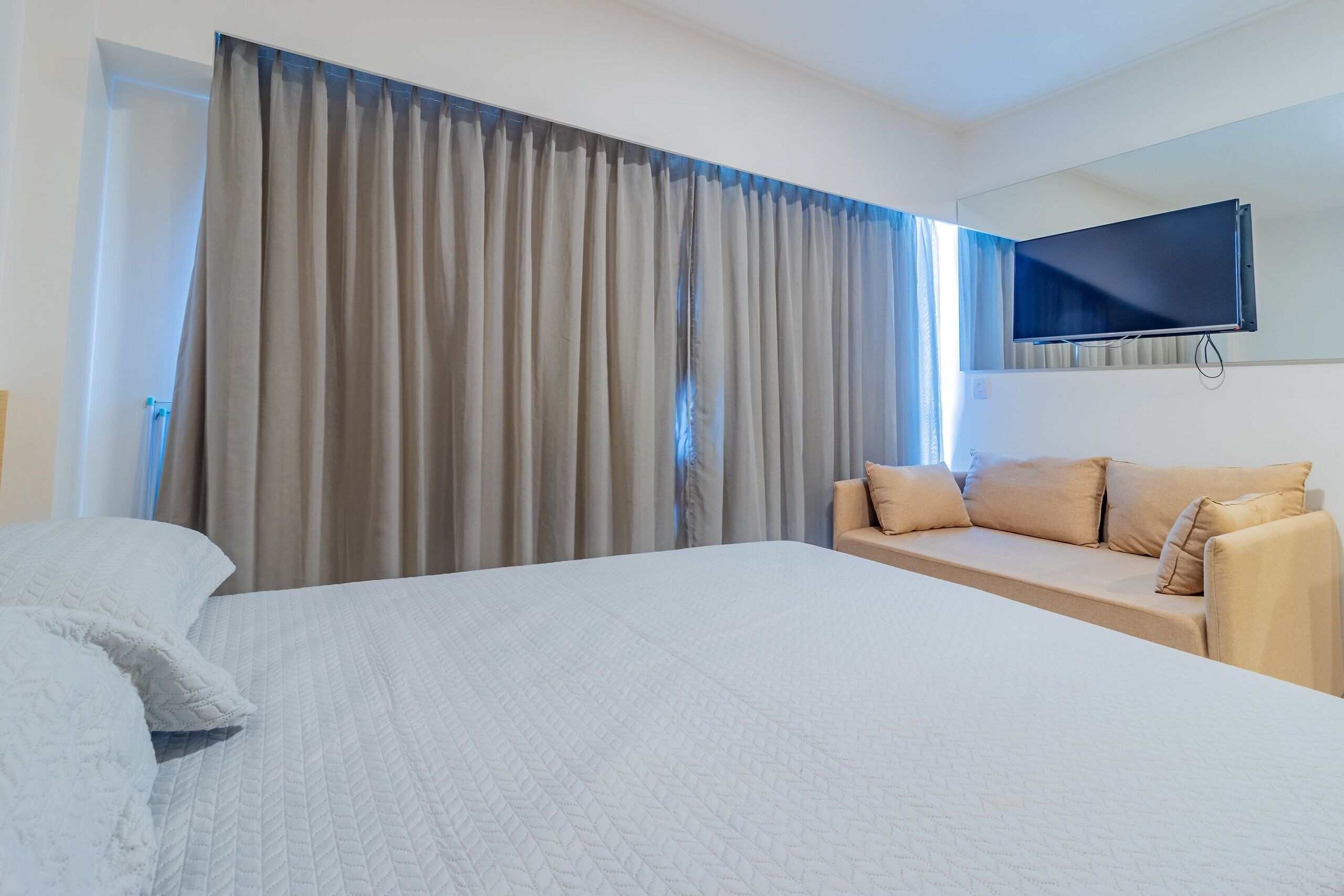 Camera d'albergo con un letto grande, un divano, una TV a schermo piatto montata a parete e una finestra con tende.