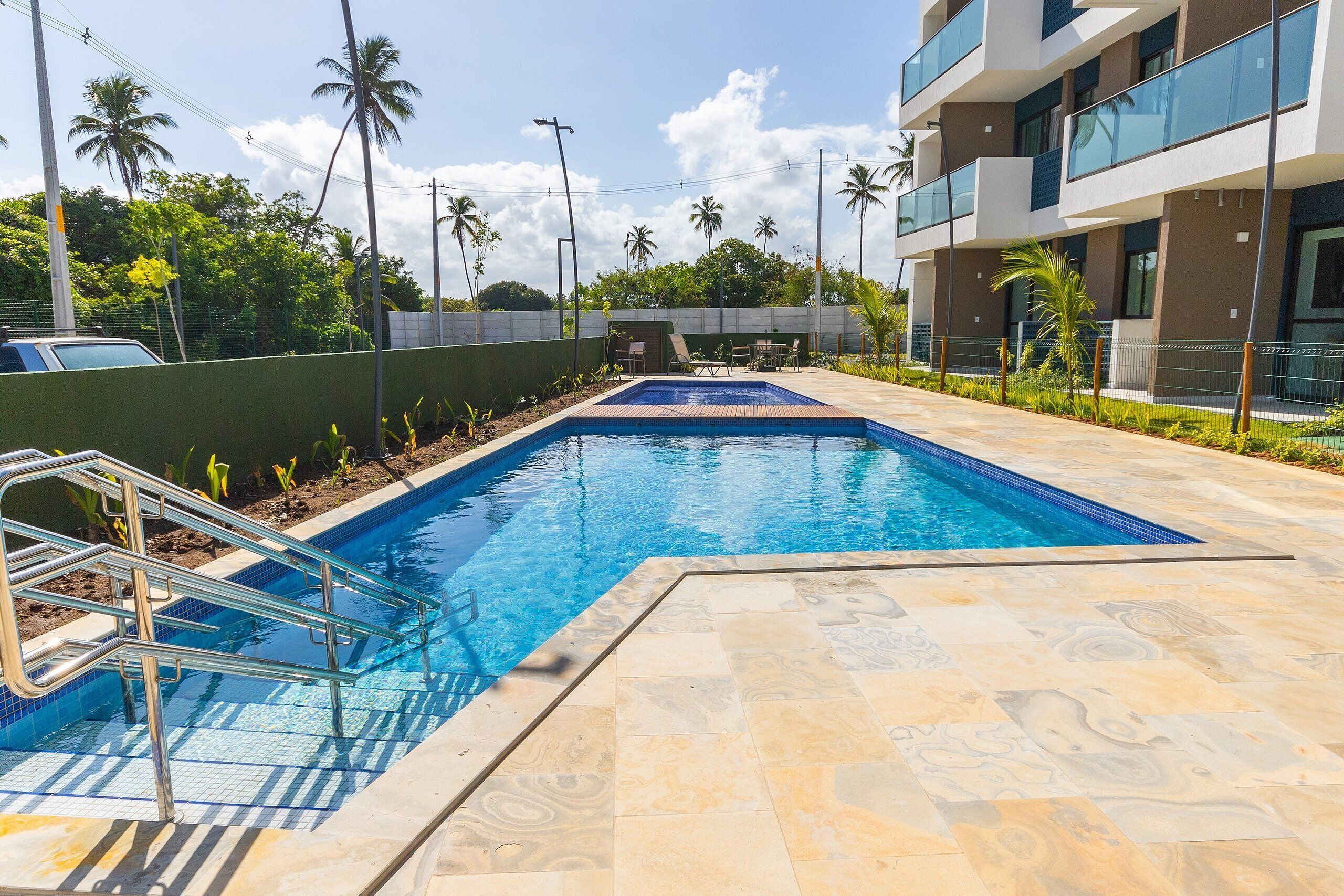 A swimming pool with a tiled deck, surrounded by a low wall and palm trees.