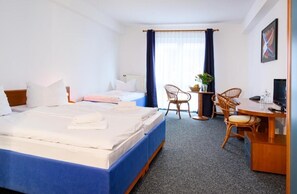 Une chambre d’hôtel comprenant un lit, un bureau avec une chaise, une télévision et une fenêtre avec des rideaux.