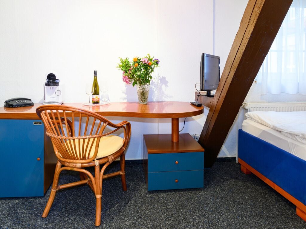 Ein Hotelzimmer mit Bett, Schreibtisch mit Stuhl, einem kleinen Tisch mit Blumenvase, Fernseher und Telefon.