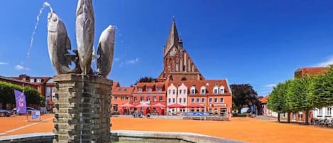 A fountain with fish sculptures in a square with buildings in the background.