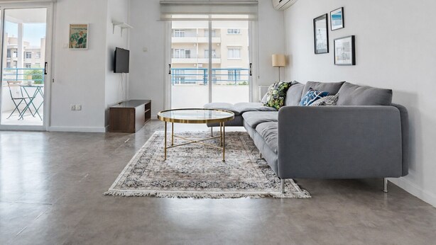 Ein modernes Wohnzimmer mit einem grauen Sofa, einem Glastisch und einem gemusterten Teppich.