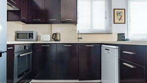 Eine moderne Küche mit dunklen Schränken, Edelstahlgeräten und einem Fenster mit Jalousien.