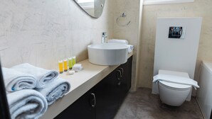 Ein Badezimmer mit rundem Waschbecken, einem Spiegel, einer Toilette und einem Handtuchhalter.
