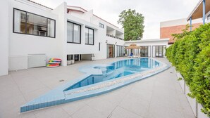 Un edificio moderno con piscina, mobiliario exterior y un gran árbol.