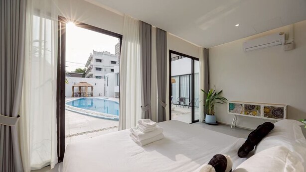 Una habitación de hotel con una cama grande, vistas a una piscina y un balcón con mobiliario exterior.