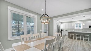 Una cocina moderna con armarios blancos, una isla central y un comedor con mesa y sillas blancas.