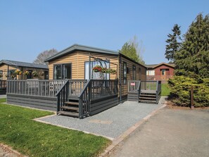 Een houten vakantiebungalow met terras, klein portaal en een oprit met grind.
