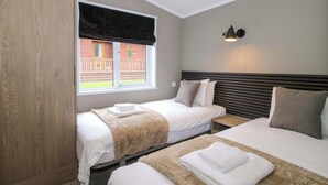 Een slaapkamer met twee bedden, een garderobe, een raam met uitzicht op een gebouw en een wandlamp.
