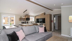 Een moderne woonkamer met een grijze bank, een houten salontafel en een keuken met houten kasten en een televisie.