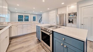 Een moderne keuken met witte en blauwe kastjes, roestvrijstalen apparatuur en een marmeren aanrecht.