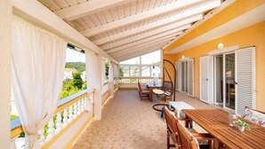 A covered outdoor area with a wooden table and chairs, a view of greenery outside, and a yellow wall. - Apartments Foric (Rab)