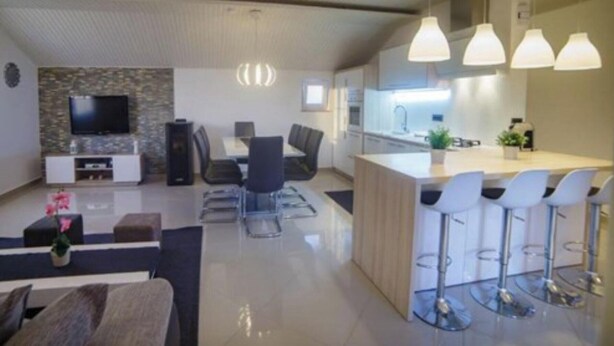 A modern kitchen with a central island, bar stools, and pendant lighting. - Apartments Foric (Rab)
