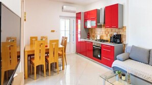 A modern kitchen with red cabinets, a dining area with wooden chairs, and a glass coffee table. - Apartments Foric (Rab)